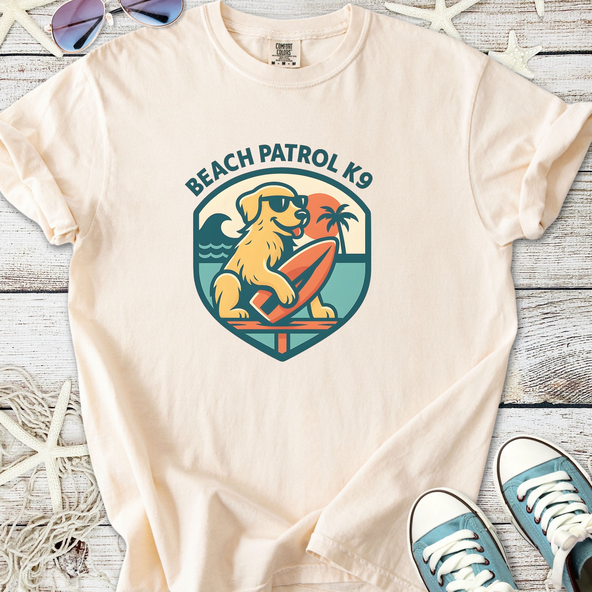 Light beige t-shirt featuring a Beach Patrol K9 graphic with a dog, surfboard, and palm tree.