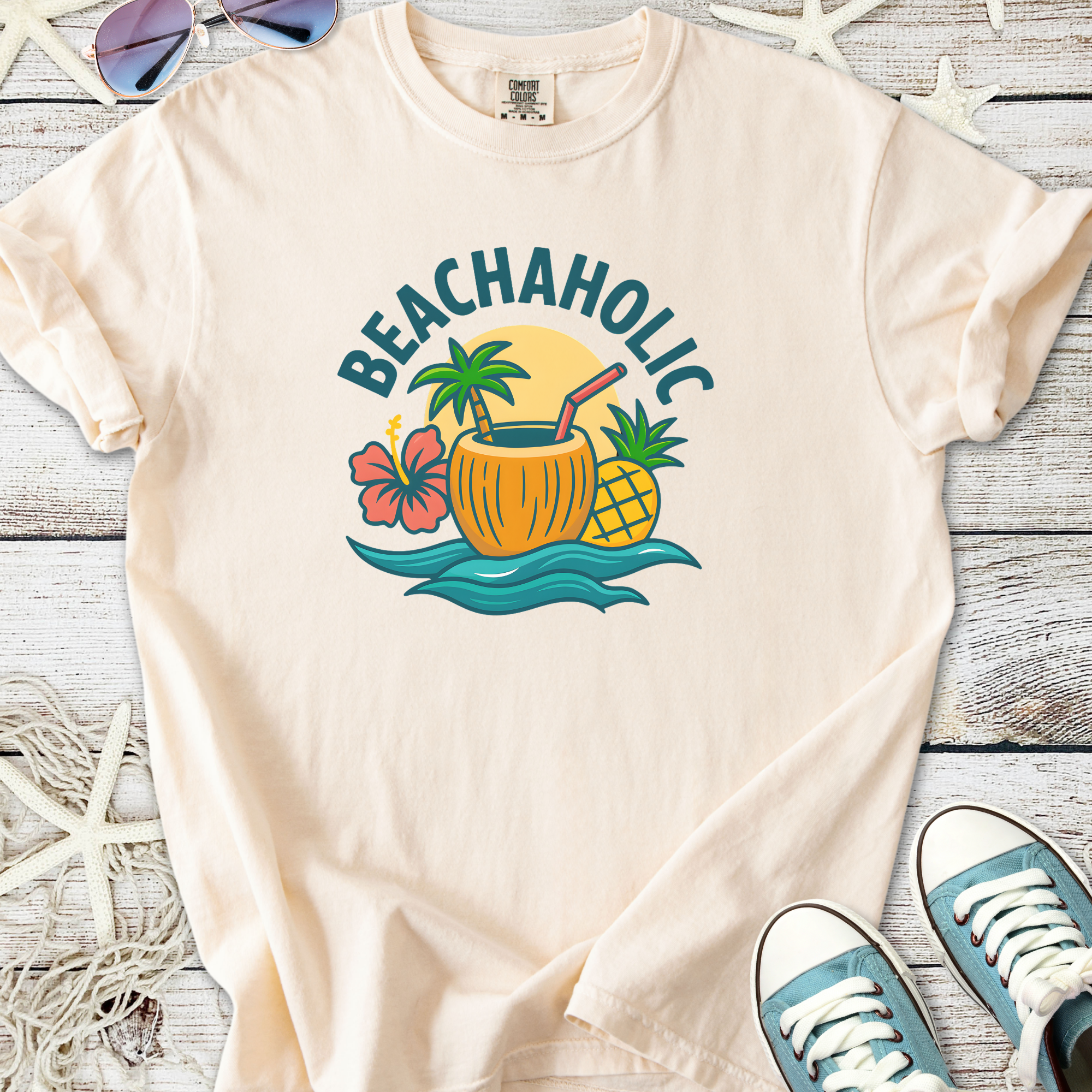 Cream t-shirt featuring 'BEACHAHOLIC' design with tropical drink, hibiscus, and pineapple graphics.