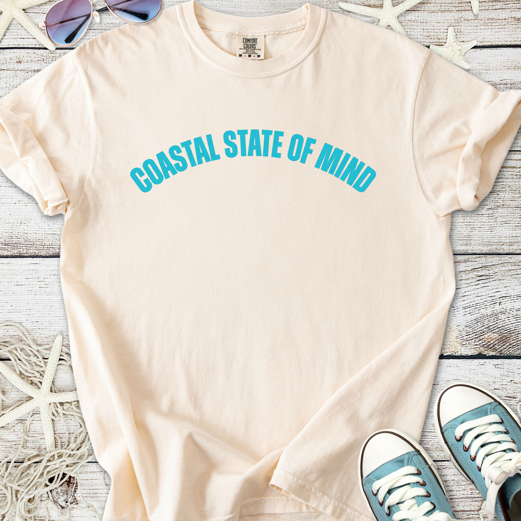 Light beige cotton t-shirt with 'Coastal State of Mind' graphic in turquoise, perfect for casual beachwear.