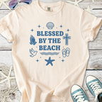 Peach-colored t-shirt featuring 'Blessed by the Beach' graphic with seashells and beach elements.