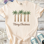 Light peach t-shirt featuring palm trees with holiday lights and 'Merry Christmas' text, perfect for festive vibes.