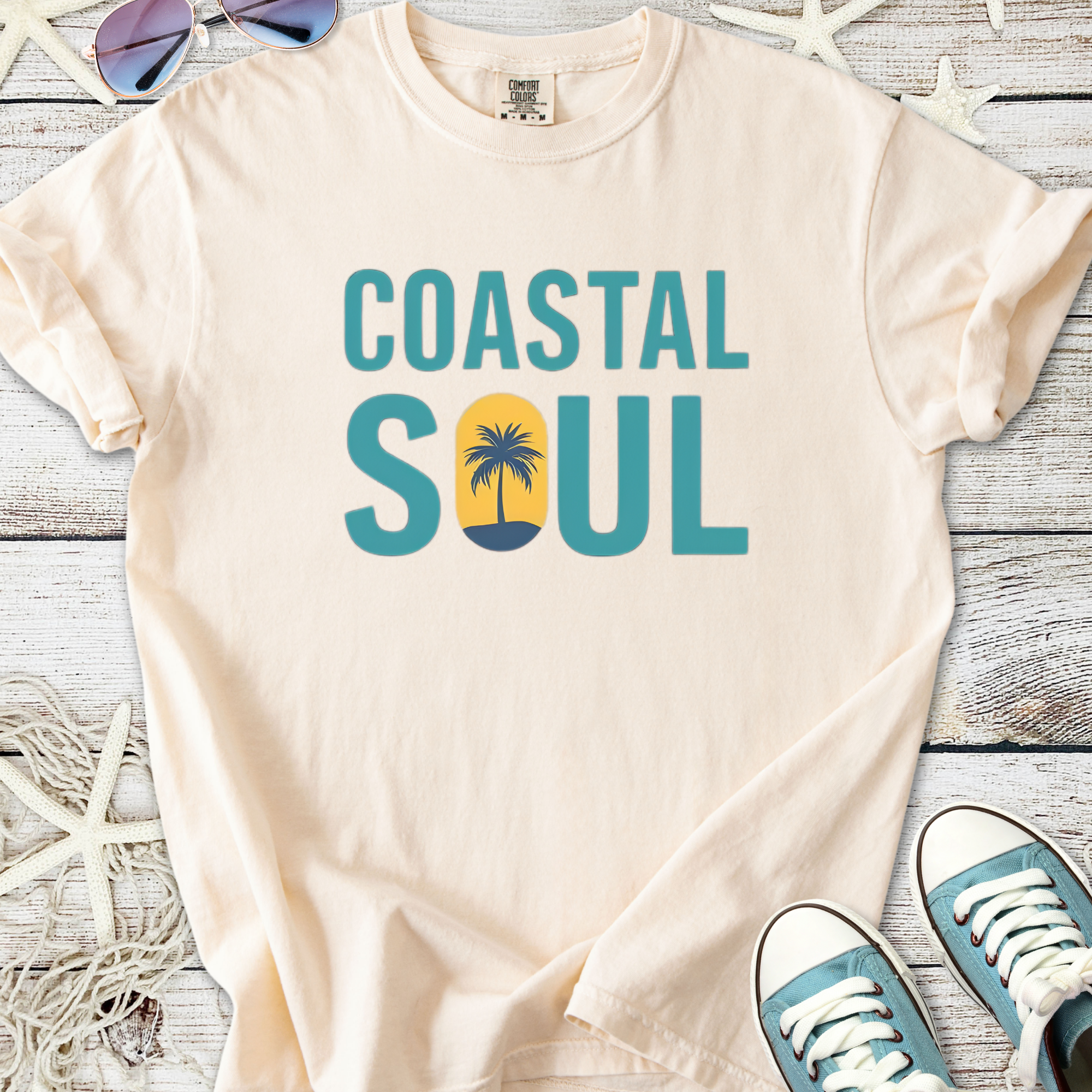 Light beige t-shirt with 'Coastal Soul' graphic and palm tree design, perfect for beach lovers.
