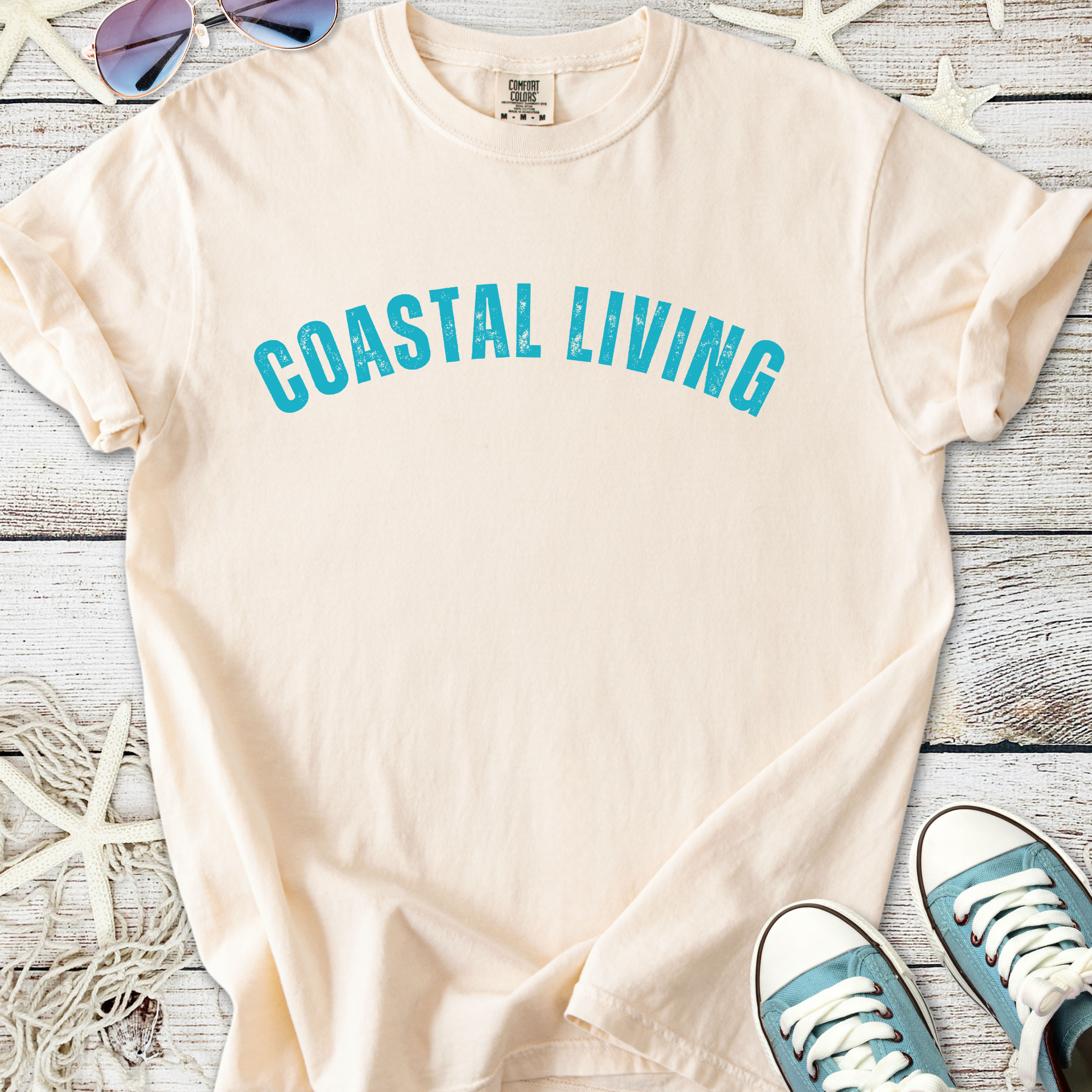 Beige cotton t-shirt with 'Coastal Living' print in teal, perfect for casual beachwear.