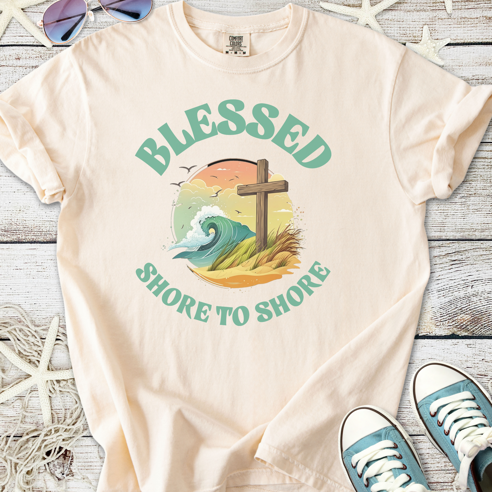 Cream graphic t-shirt featuring 'Blessed Shore to Shore' design with ocean wave and cross.