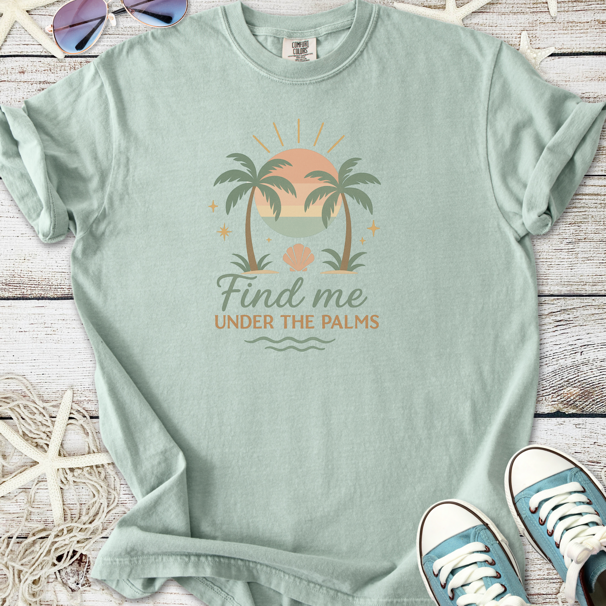 Mint green graphic tee featuring palm trees and sunset design with 'Find me Under the Palms' text.