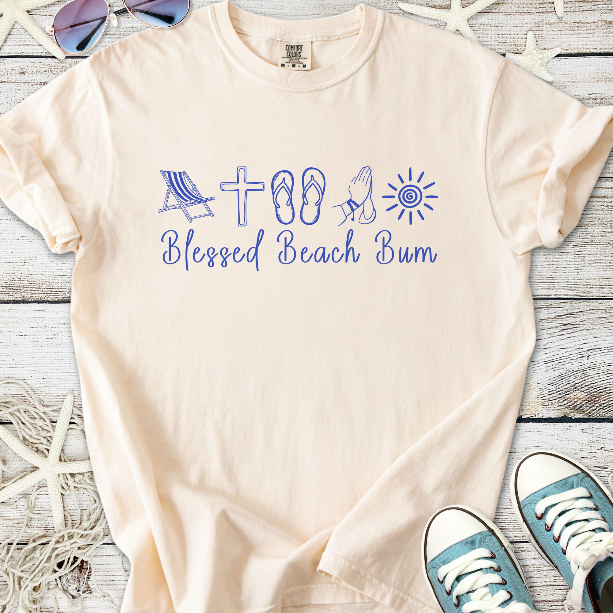 Light beige t-shirt with 'Blessed Beach Bum' graphic in blue, featuring beach icons like a chair and flip-flops.