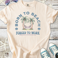 Light peach t-shirt with 'Born to Beach, Forced to Work' graphic, featuring palm trees and a hammock.