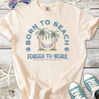 Light peach t-shirt with 'Born to Beach, Forced to Work' graphic, featuring palm trees and a hammock.
