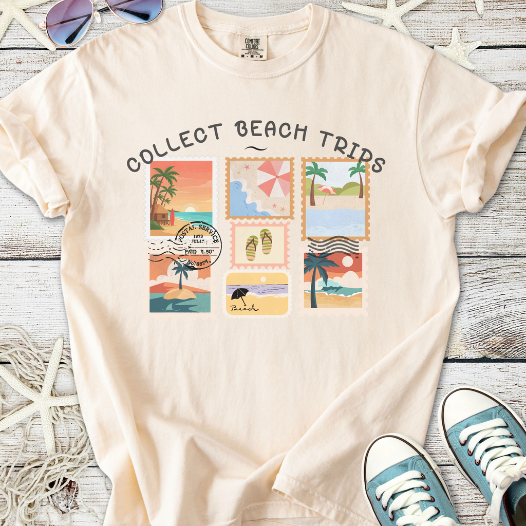 Beige graphic t-shirt featuring 'Collect Beach Trips' with colorful postcard designs and beach illustrations.