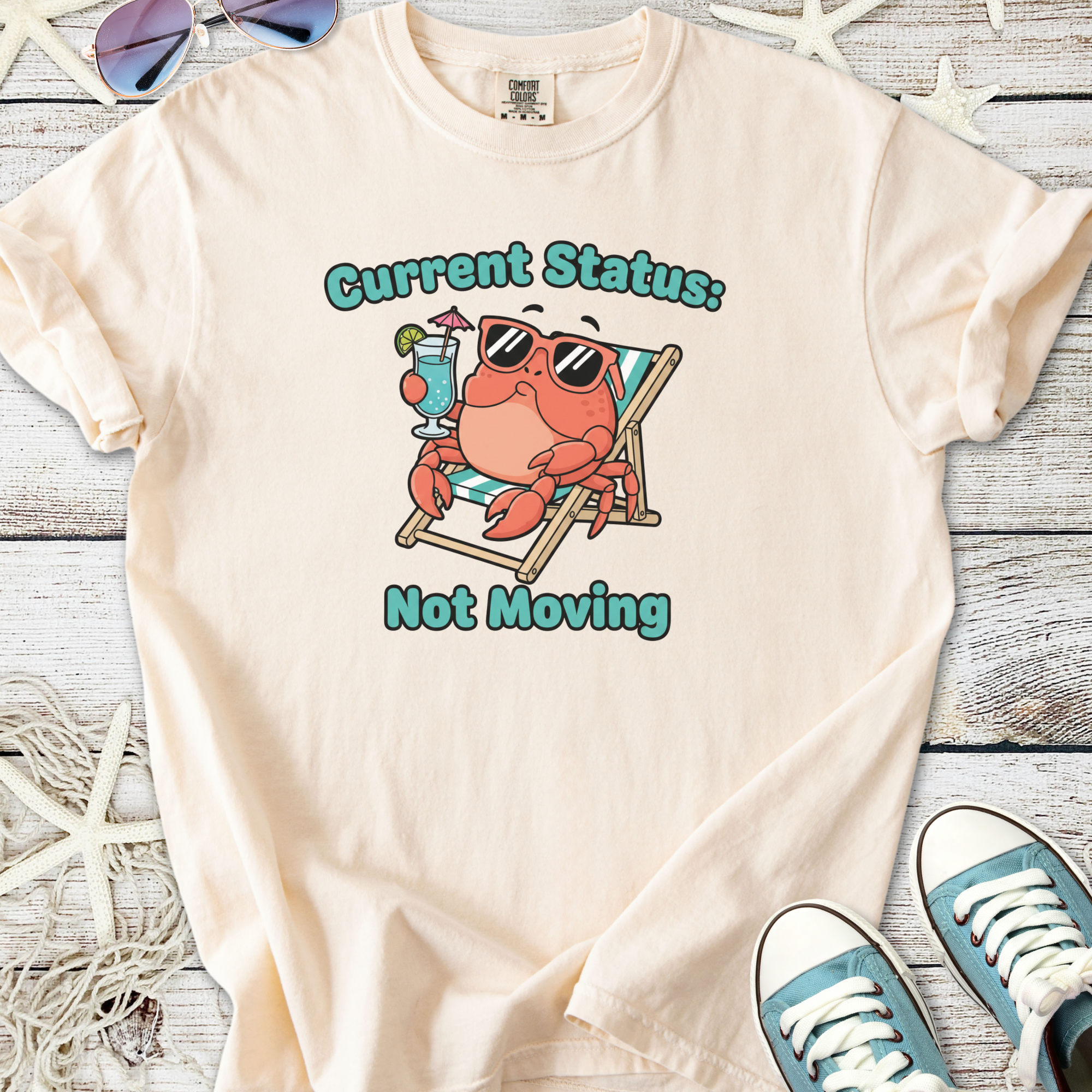Cream t-shirt featuring a relaxed cartoon crab with sunglasses, drink, and text 'Current Status: Not Moving'.