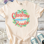 Beige 'Christmas in Paradise' t-shirt, featuring a tropical design with greenery and beach scene.