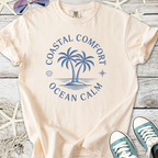 Beige cotton t-shirt featuring a coastal graphic with palm trees and ‘Ocean Calm’ text, perfect for beach lovers.