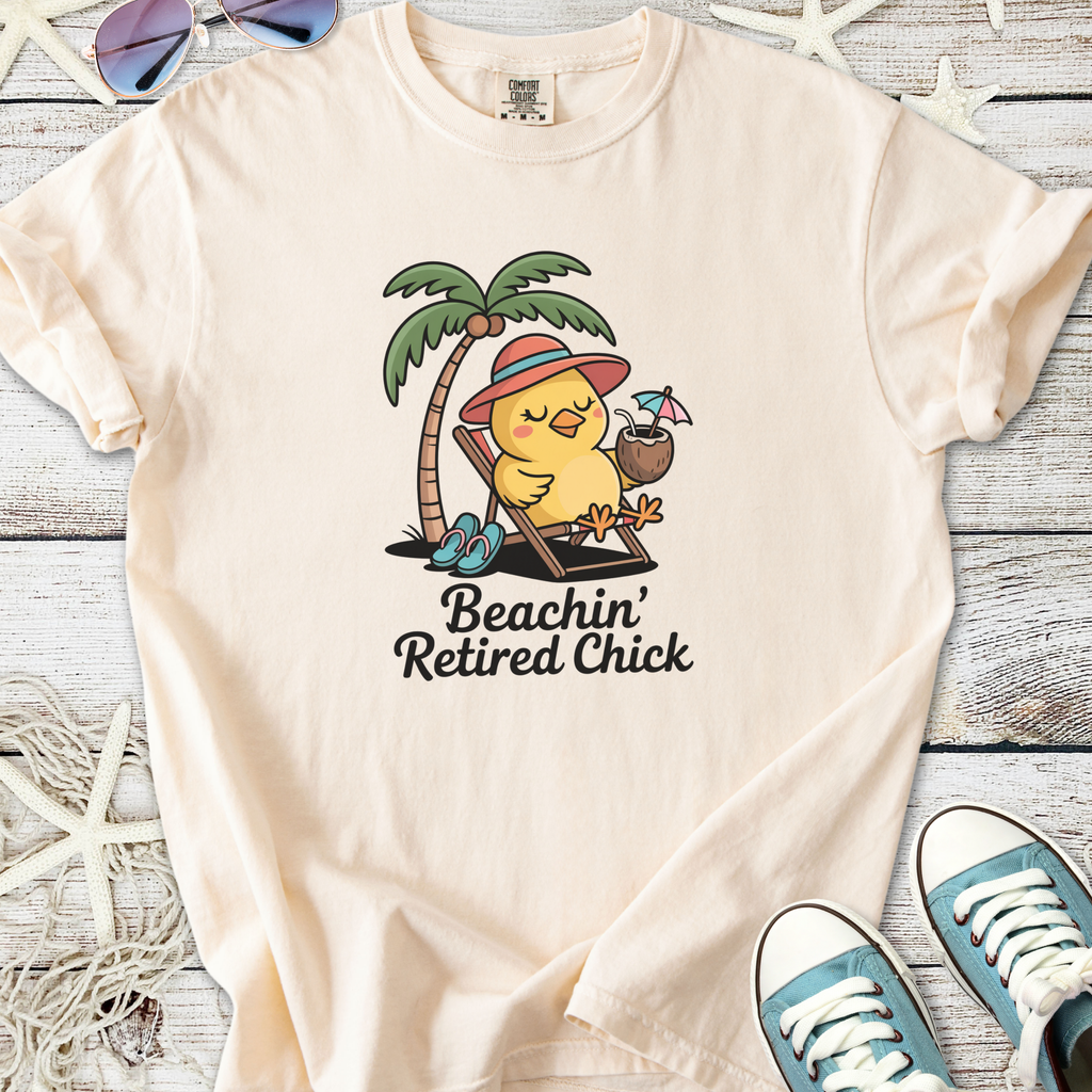 Peach-colored t-shirt featuring a cute chick under a palm tree, sipping a drink, labeled 'Beachin’ Retired Chick'.