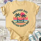 Beige graphic tee featuring palm trees and hammock with the phrase 'Another Day, Another Beach Nap'.