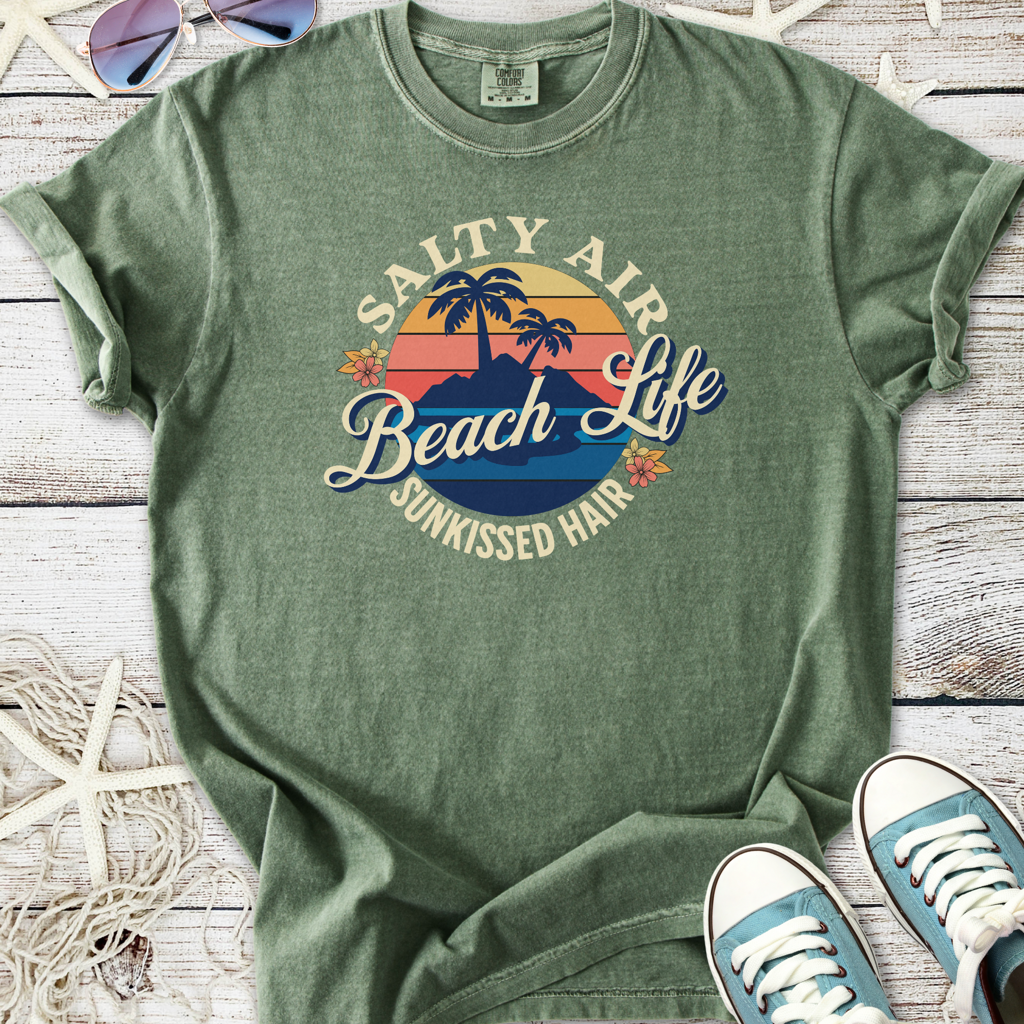 Green cotton t-shirt featuring 'Salty Air Beach Life' graphic with palm trees and sunset design.