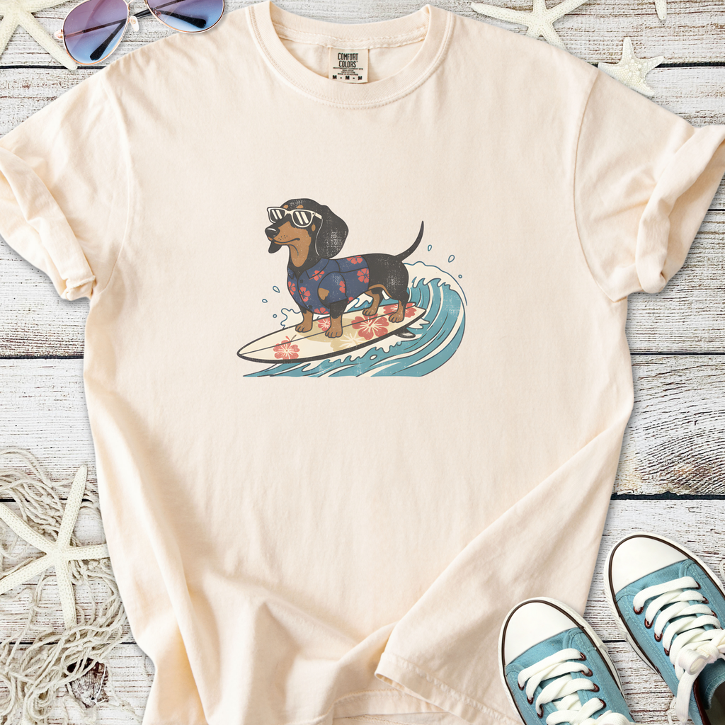 Light beige t-shirt featuring a cartoon dachshund in sunglasses surfing on a wave, perfect for dog lovers.