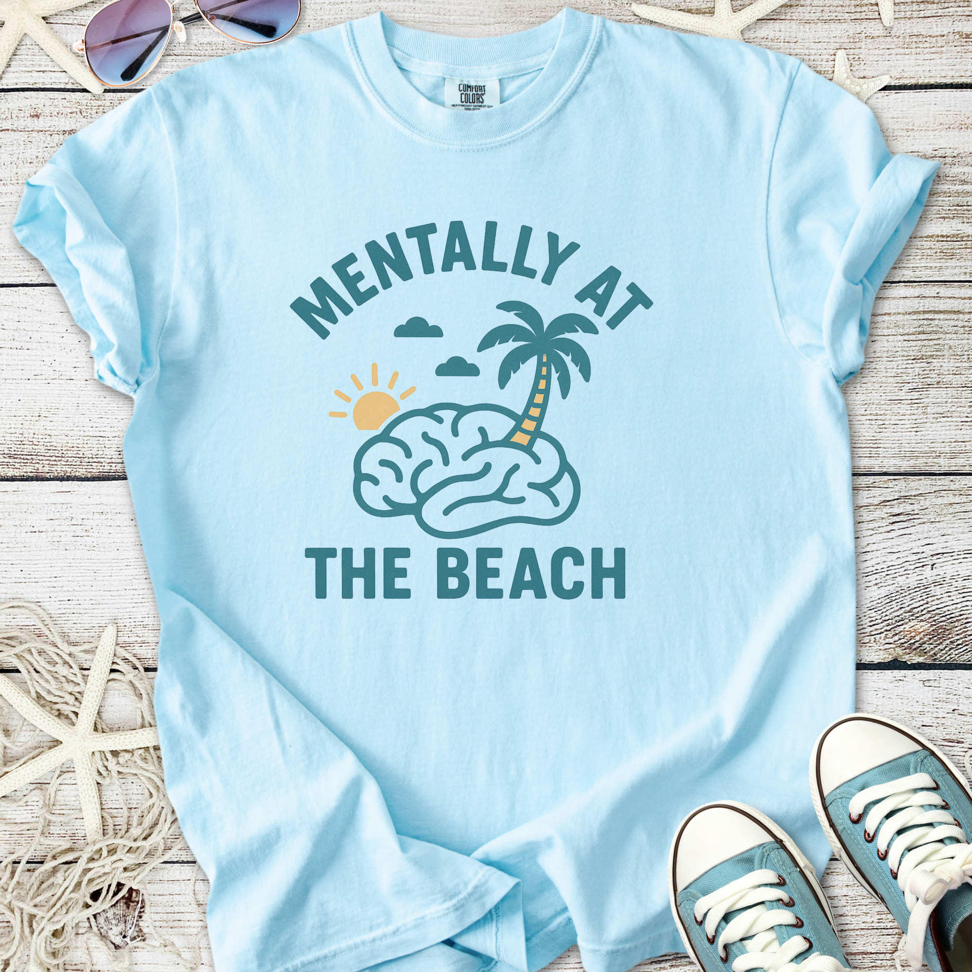 Light blue t-shirt with 'Mentally at the Beach' graphic, featuring a brain, palm tree, and sun.