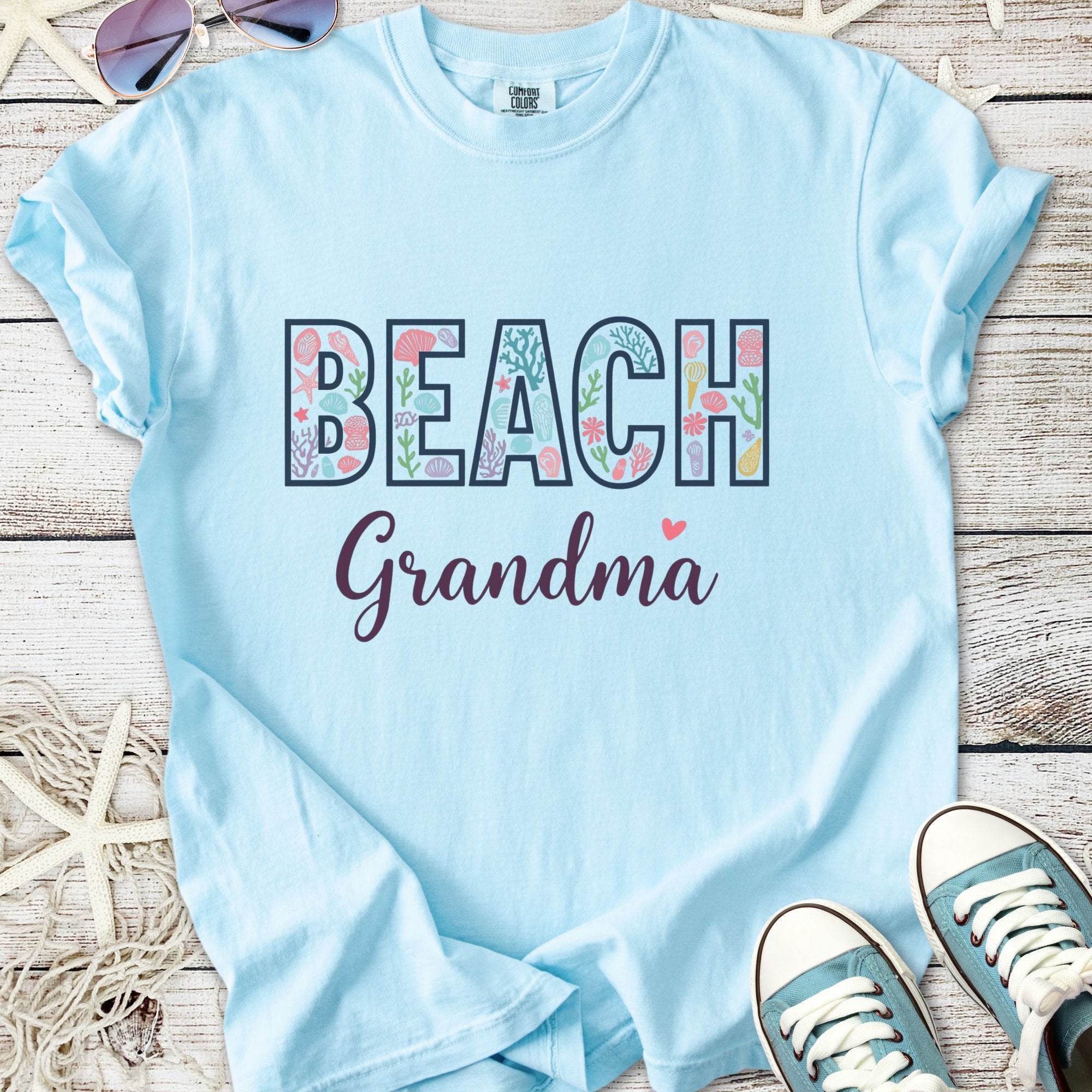 Light blue t-shirt with 'BEACH Grandma' text featuring floral and marine designs, perfect for summer.
