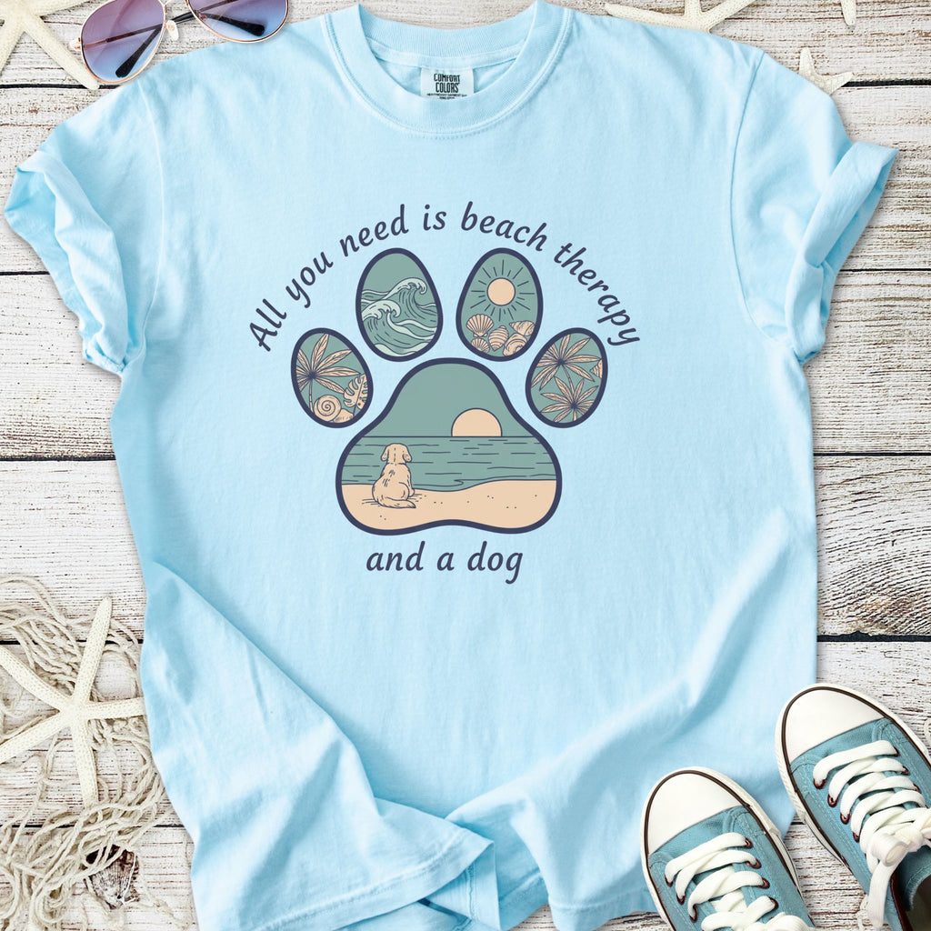 Light blue t-shirt with a beach-themed graphic: paw print design featuring waves, sun, and dog.