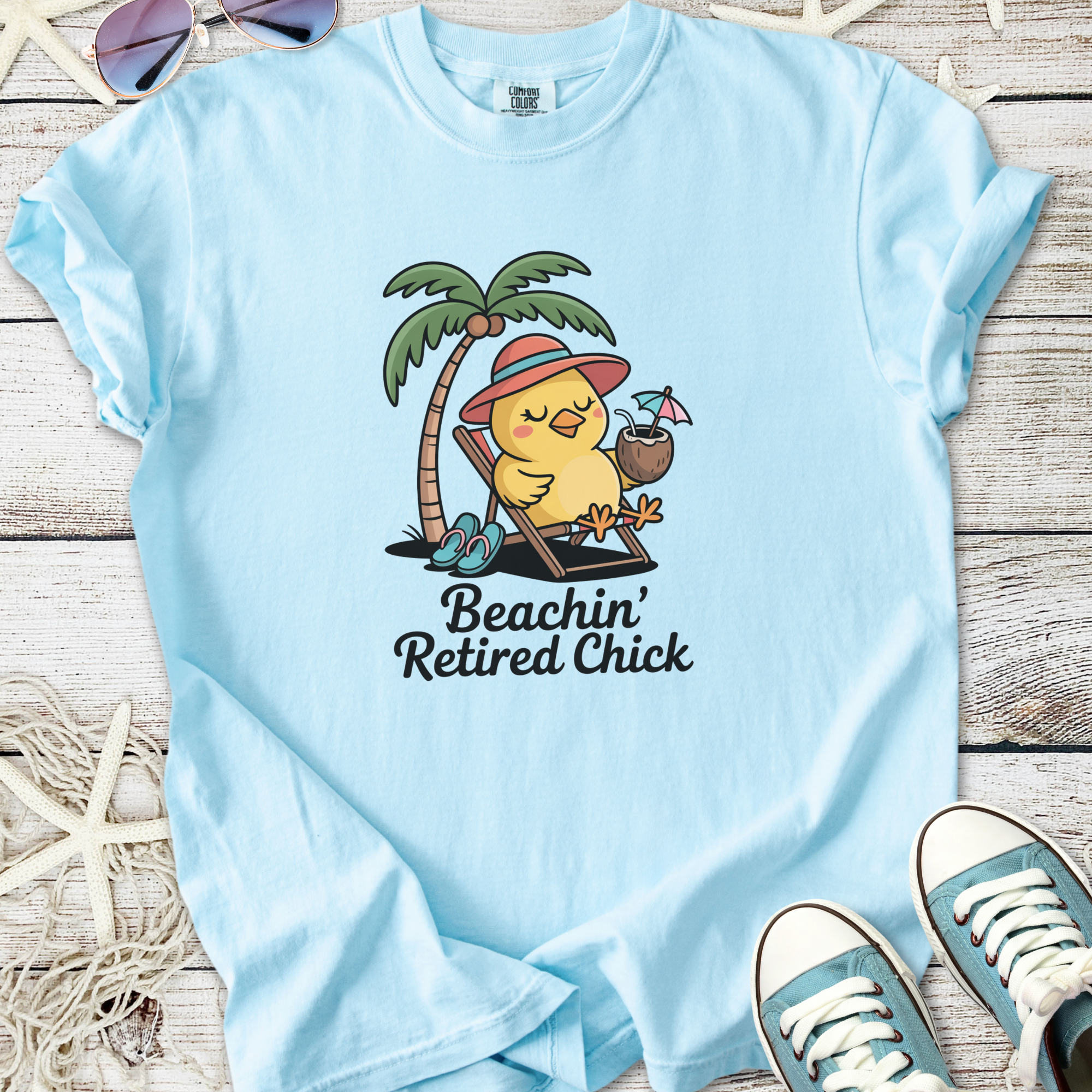 Light blue t-shirt featuring a cute cartoon chick relaxing under a palm tree with a drink.