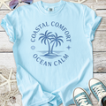 Light blue t-shirt featuring palm tree graphic and 'Coastal Comfort Ocean Calm' text, perfect for summer.