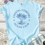 Light blue t-shirt featuring palm tree graphic and 'Coastal Comfort Ocean Calm' text, perfect for summer.