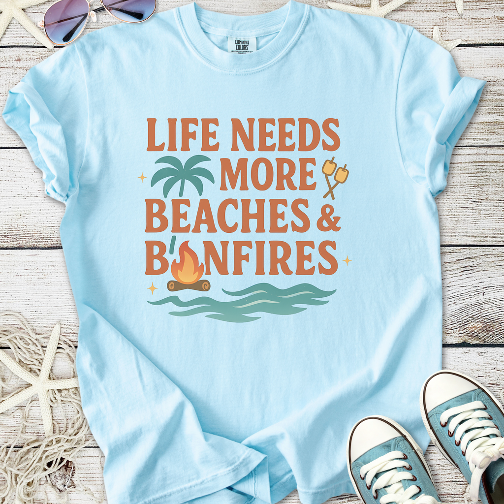 Light blue graphic t-shirt with 'Life Needs More Beaches & Bonfires' design, perfect for beach lovers.