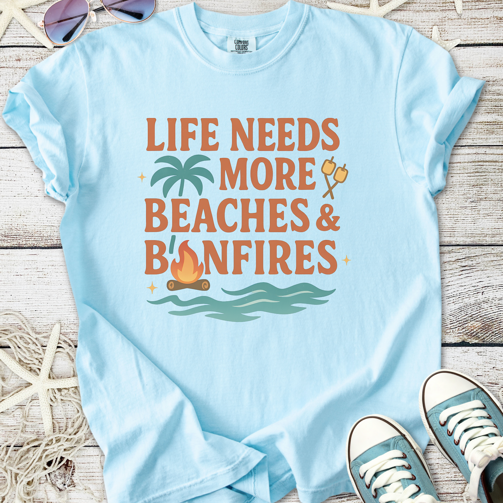 Light blue graphic t-shirt with 'Life Needs More Beaches & Bonfires' design, perfect for beach lovers.
