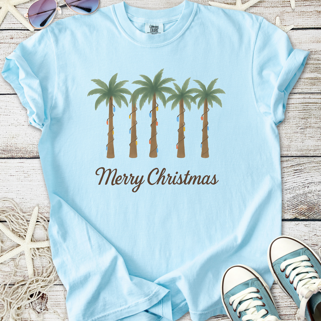 Light blue Christmas t-shirt featuring palm trees with colorful lights and 'Merry Christmas' text.