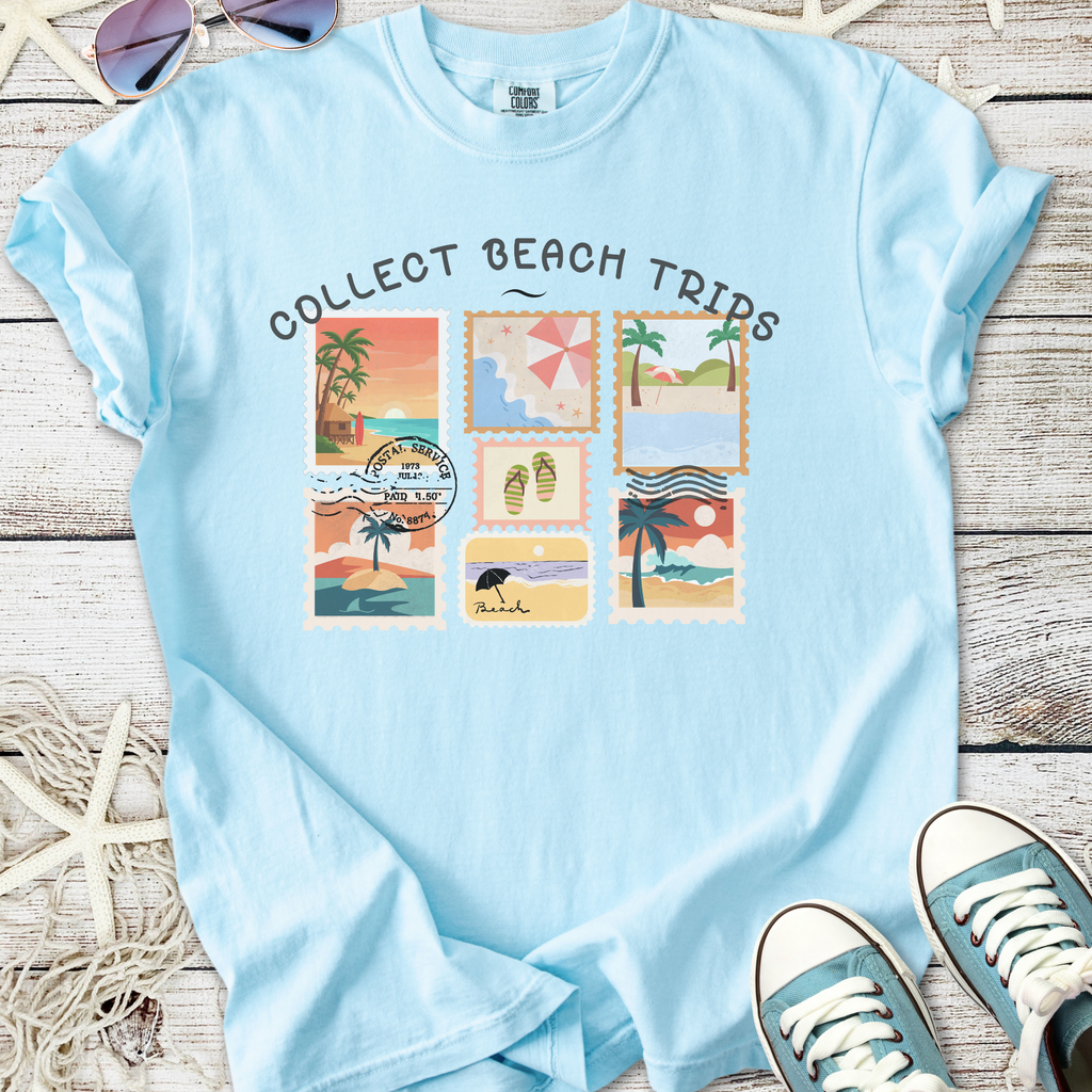 Light blue graphic tee featuring beach stamp designs and 'Collect Beach Trips' slogan.