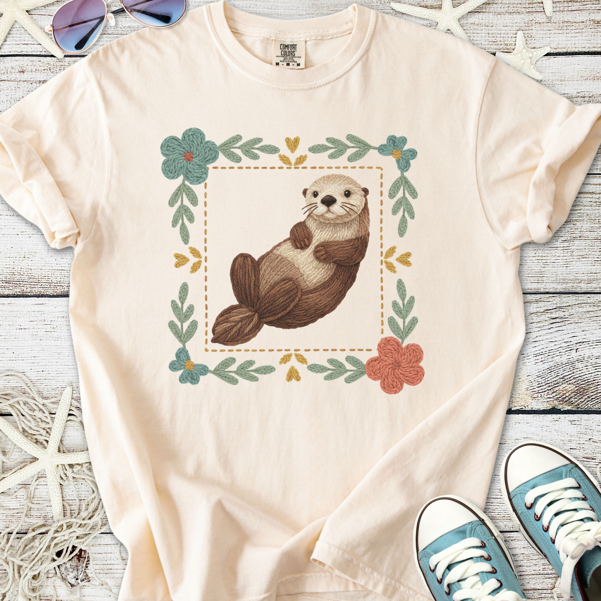 Cream t-shirt featuring a cute otter design surrounded by floral accents, perfect for casual wear.