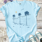 Light blue t-shirt featuring a beach scene with palm trees, moon, and string lights, perfect for summer.