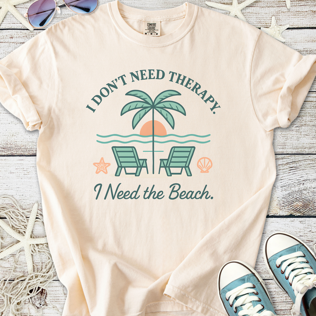 Cream t-shirt with 'I Need the Beach' graphic, featuring palm trees and chairs, perfect for beach lovers.