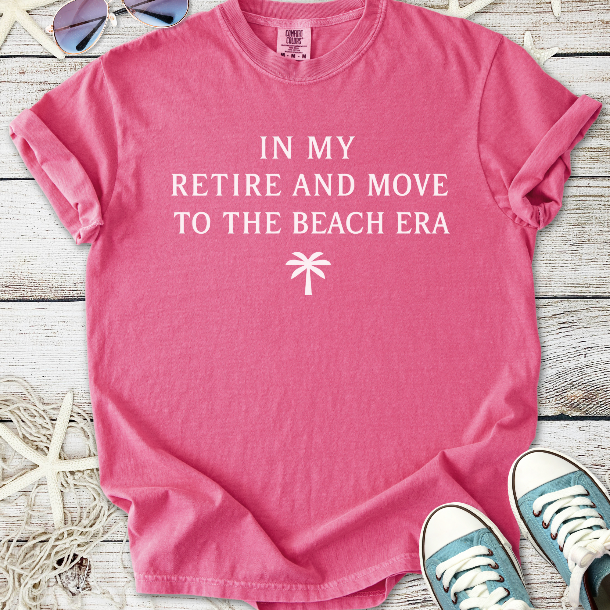 Pink cotton graphic tee with 'In My Retire and Move to the Beach Era' text and palm tree design.