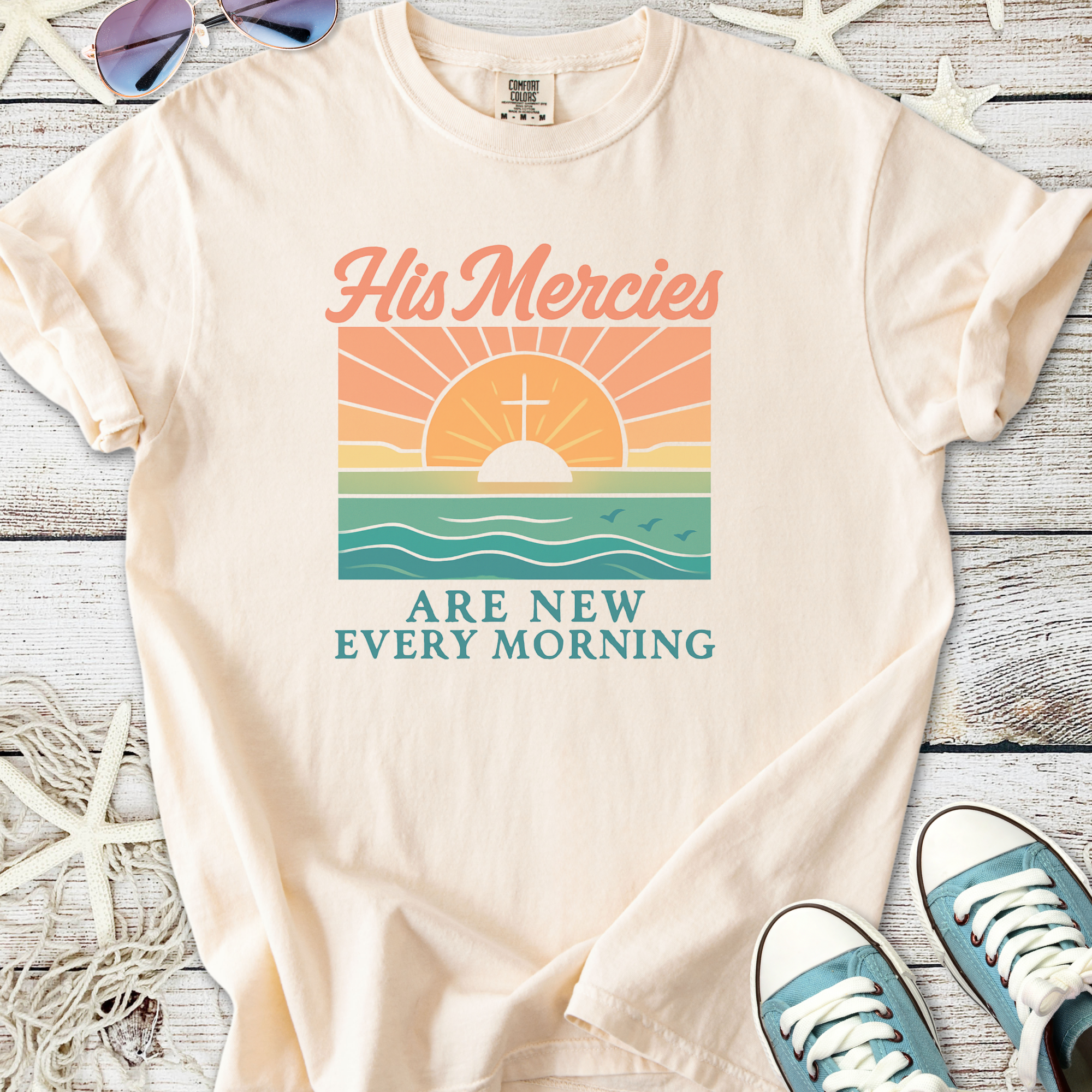 Beige graphic tee featuring sunrise design with text 'His Mercies Are New Every Morning'.