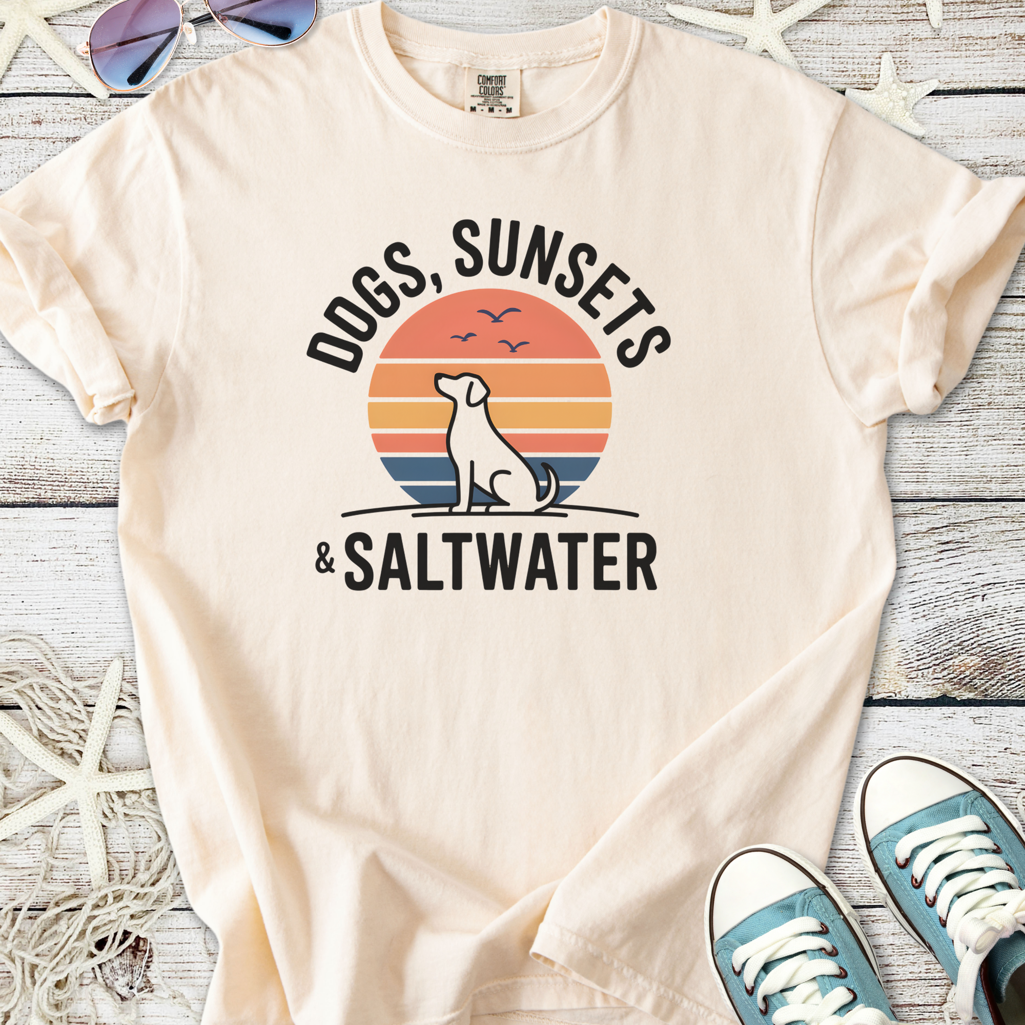 Cream t-shirt featuring a dog silhouette, sunset design, and text 'Dogs, Sunsets & Saltwater'.