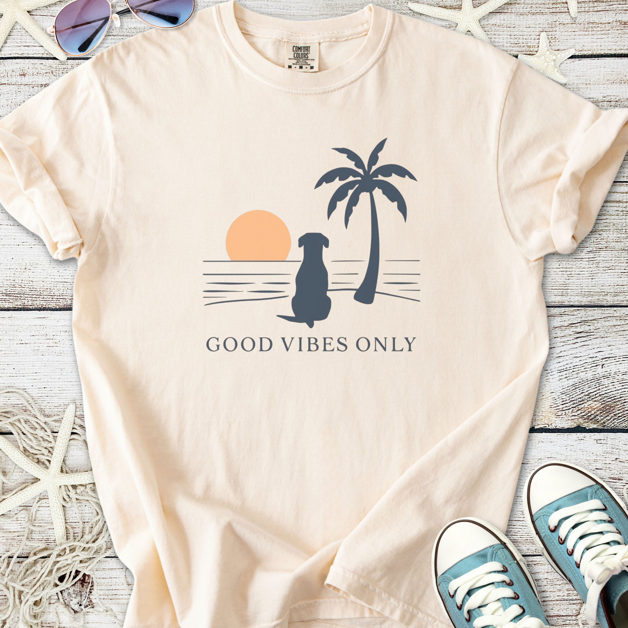 Peach graphic t-shirt featuring a dog, palm tree, sunset, and 'Good Vibes Only' text.