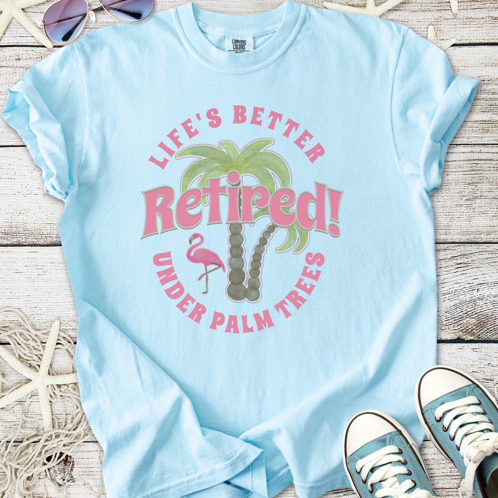 Light blue t-shirt with 'Retired!' graphic, featuring palm trees and a flamingo, perfect for retirement wear.