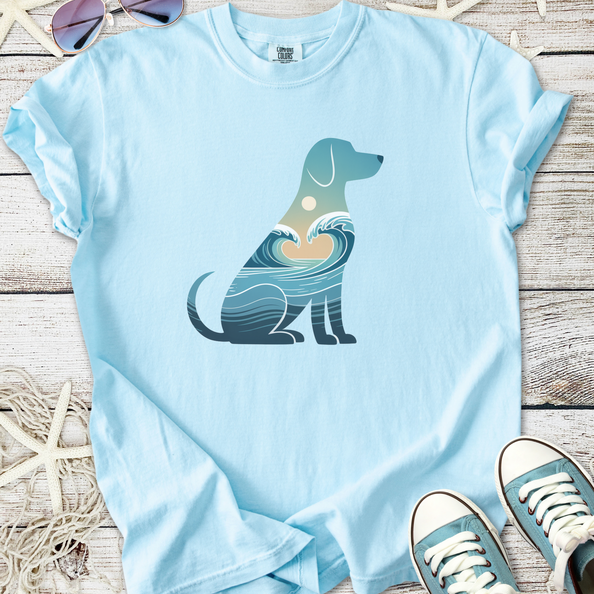 Light blue t-shirt featuring a dog silhouette with ocean waves and sun design, perfect for pet lovers.
