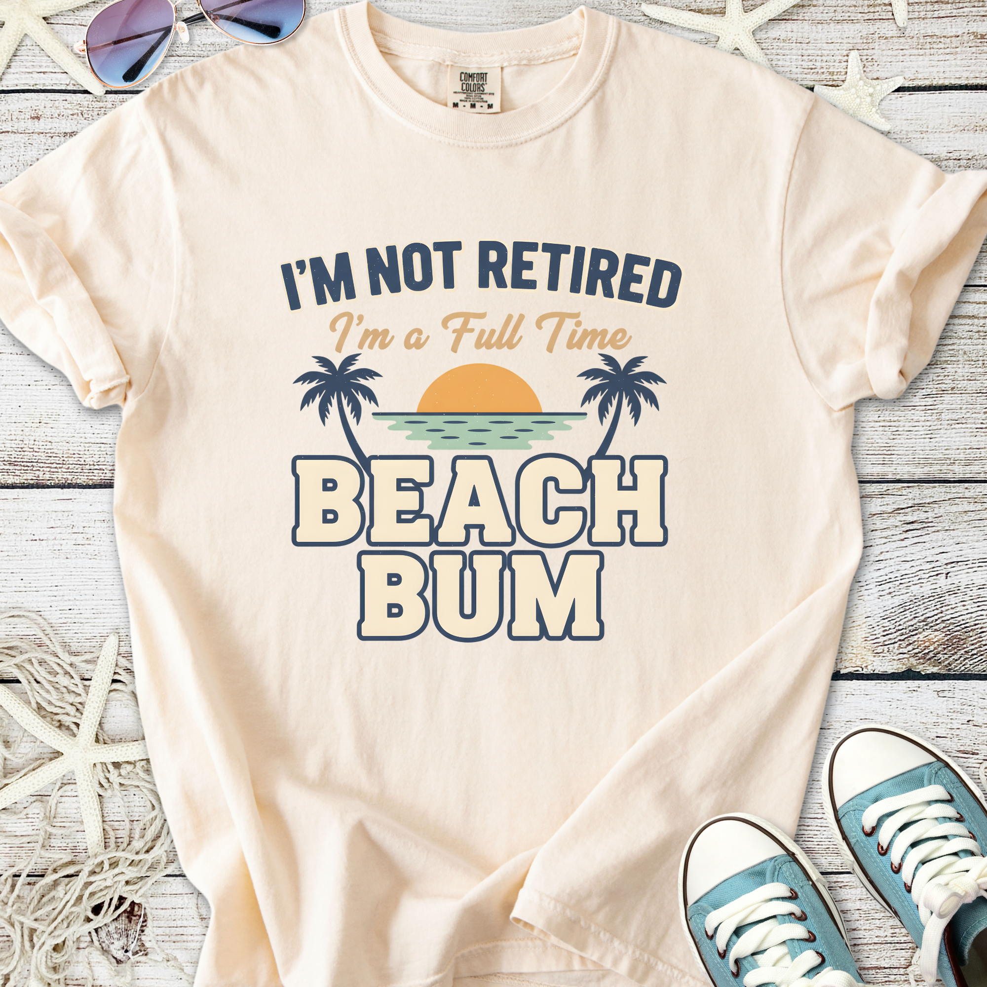 Cream graphic tee with 'I'm Not Retired, I'm a Full Time Beach Bum' design, perfect for casual beachwear.