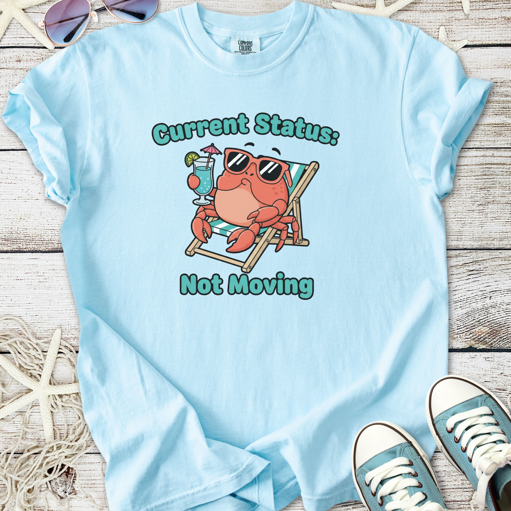 Light blue t-shirt featuring a playful crab graphic with sunglasses, lounge chair, and cocktail, ideal for summer.
