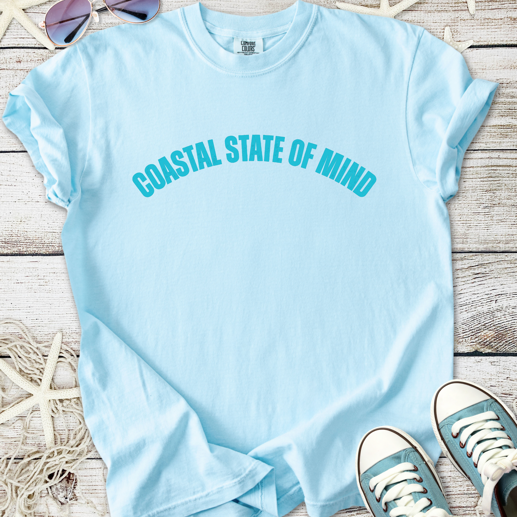 Light blue t-shirt featuring 'COASTAL STATE OF MIND' text, casual style, perfect for beach lovers.