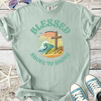 Mint green t-shirt featuring 'Blessed Shore to Shore' graphic with waves and a cross.