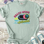 Mint green t-shirt with 'Beach Mode Activated' graphic, featuring a palm tree and sunset design.