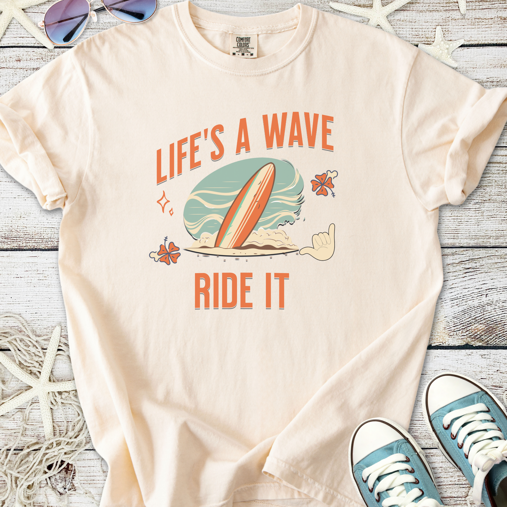Cream cotton t-shirt with 'Life's a Wave, Ride It' graphic and surfboard design, perfect for beach lovers.