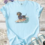 Light blue t-shirt featuring a surfing dachshund in sunglasses and a floral shirt on a wave.