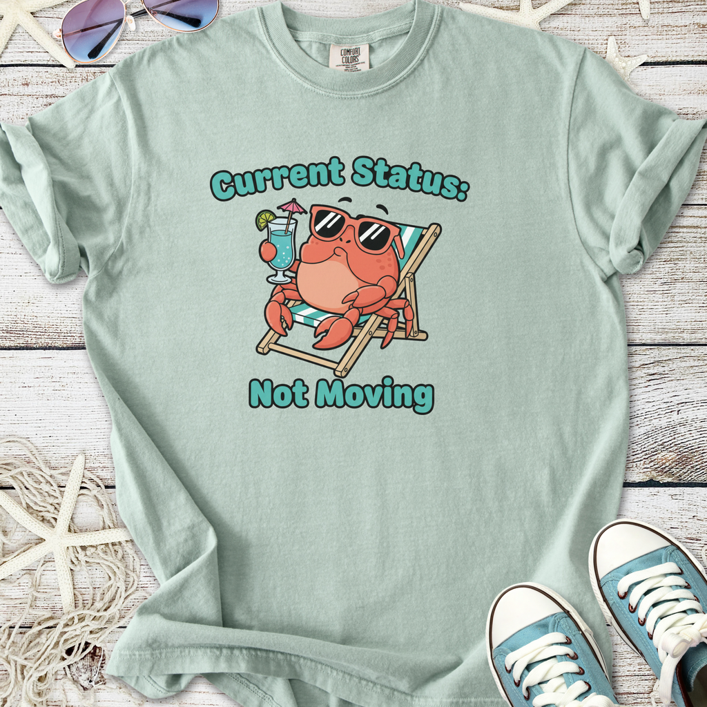 Light blue t-shirt featuring a relaxed crab graphic with sunglasses and a drink, saying 'Current Status: Not Moving'.