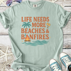Light blue t-shirt with 'Life Needs More Beaches & Bonfires' graphic, perfect for beach lovers.