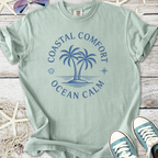 Mint green t-shirt featuring coastal comfort graphic with palm trees and ocean calm design.