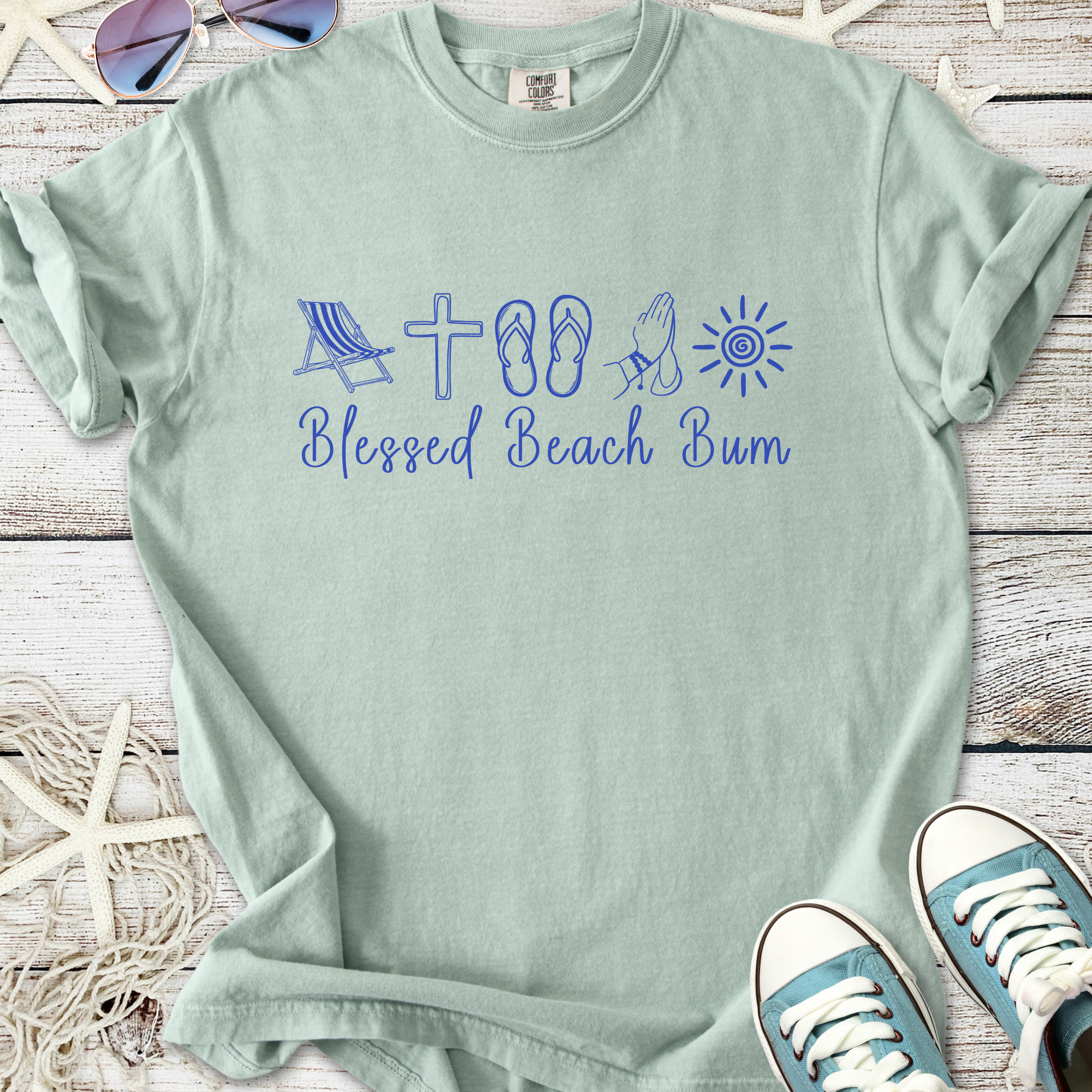 Light green t-shirt with 'Blessed Beach Bum' graphic, featuring beach icons and casual style.